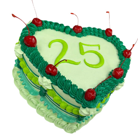 heart shaped birthday cake with green icing and maraschino cherries