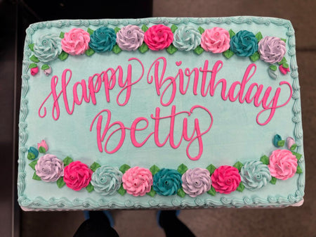 Birthday cake with 'Happy Birthday' text and floral decorations on a light blue background.
