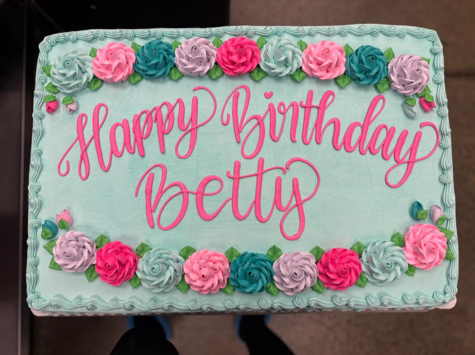 Birthday cake with 'Happy Birthday' text and floral decorations on a light blue background.