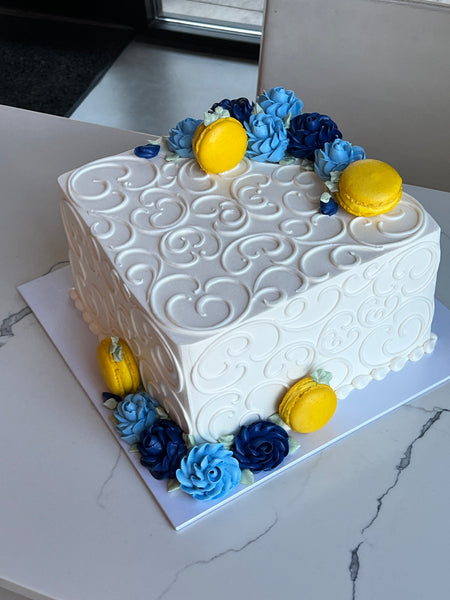 square wedding cake with scrolls, blue roses and yellow macarons